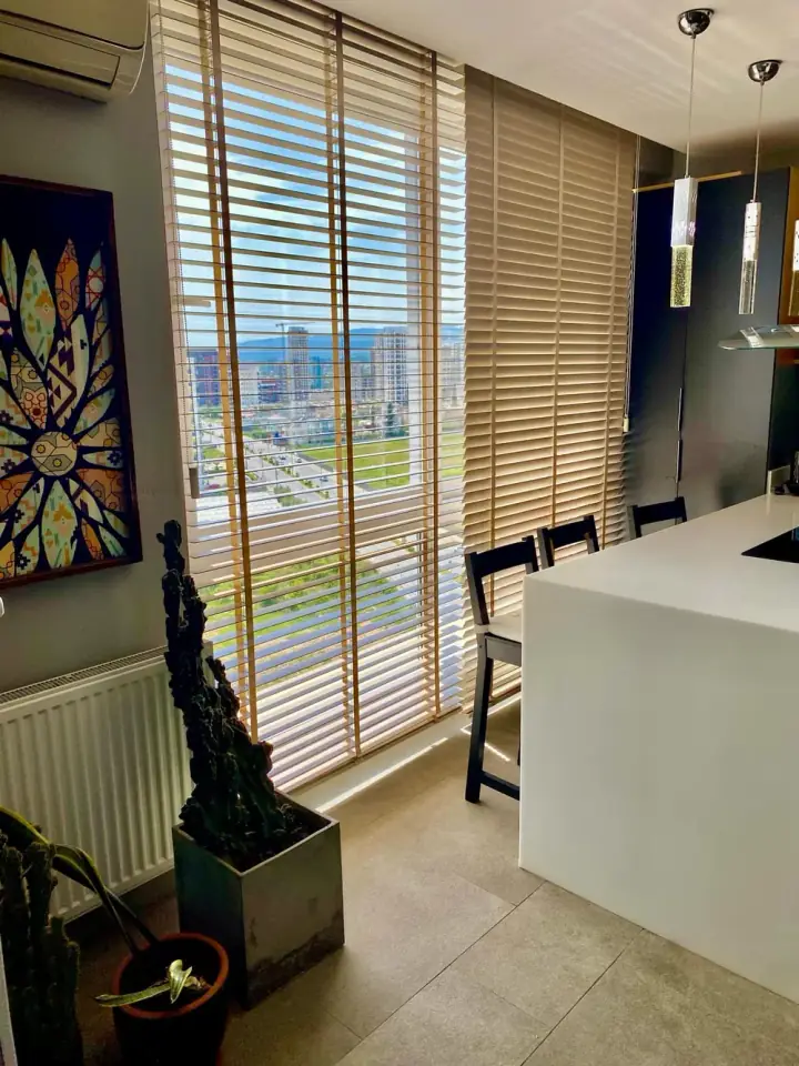 Tavandan tabana cam önünde ahşap jaluzi; şehir manzaralı salon
